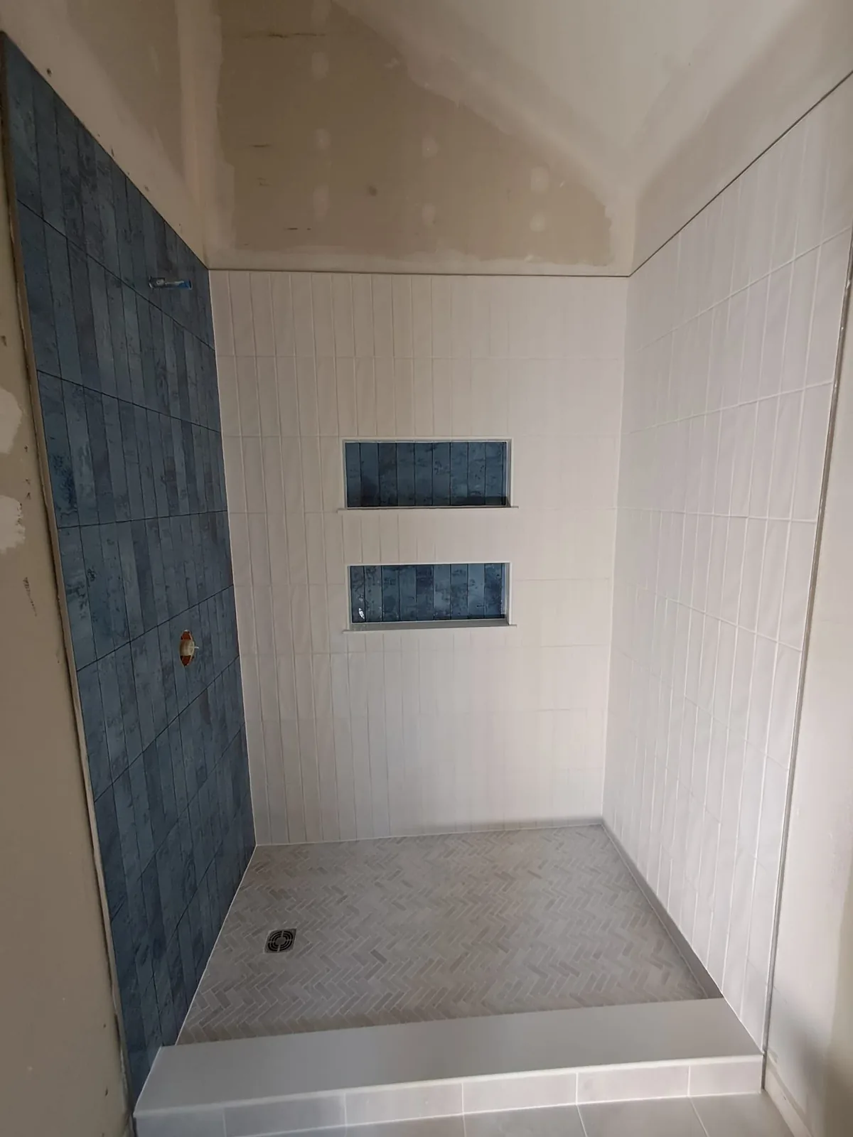 White shower with two blue tile niches and herringbone pan