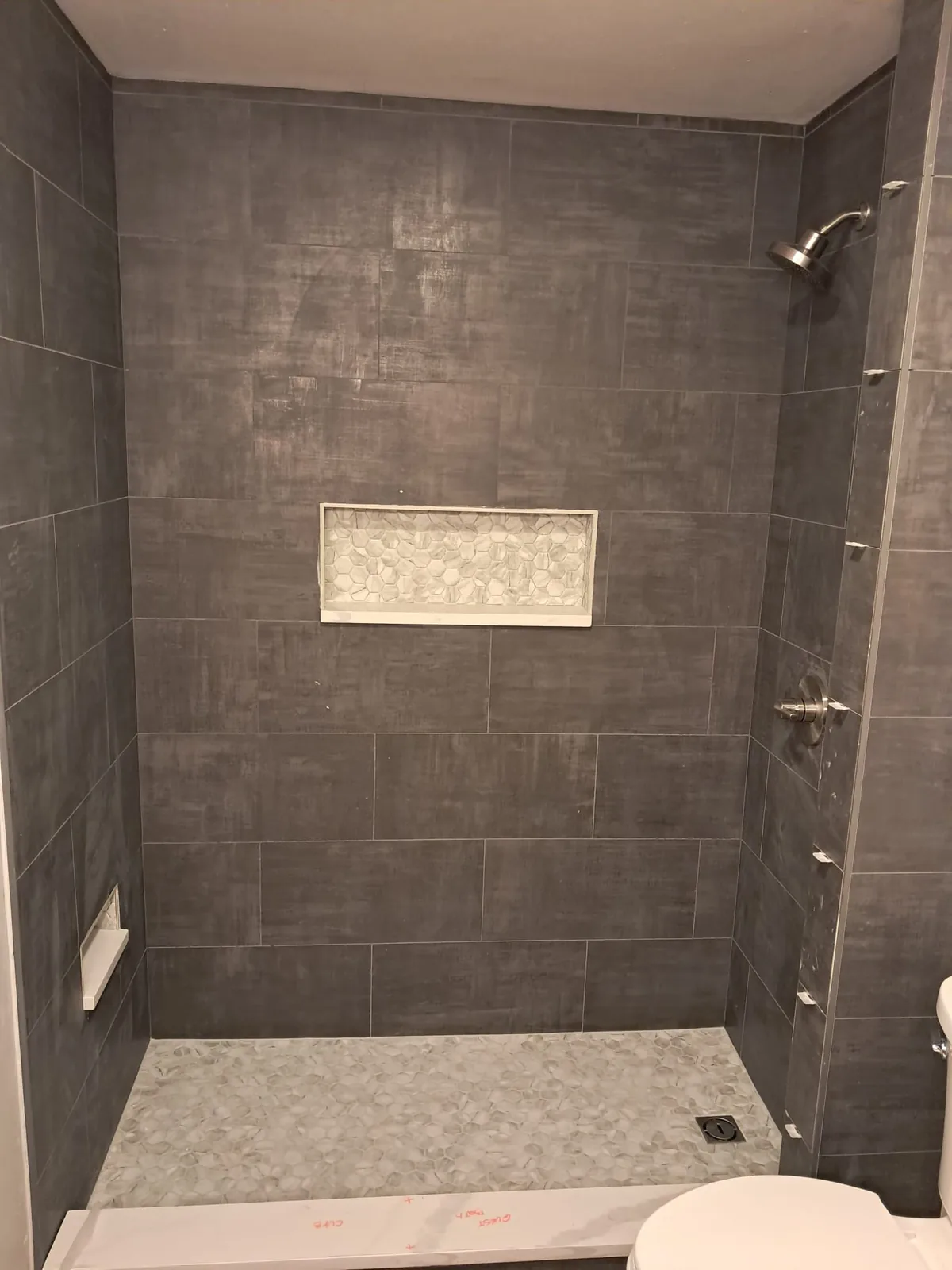 Dark tile shower with hexagon mosaic niche