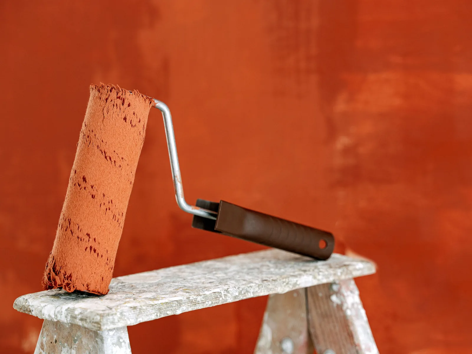 Paint roller on a ladder against a fresh orange wall